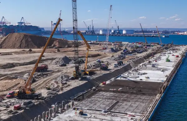 Budowa dużego portu w Japonii. Dźwigi, koparki i ciężarówki pracują na placu budowy, tworząc nową infrastrukturę.