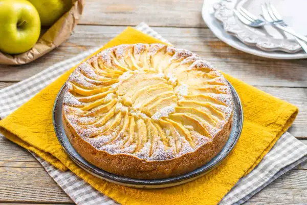 Torta di mele senza zucchero, decorata con fettine di mela disposte a raggiera e spolverata di zucchero a velo.