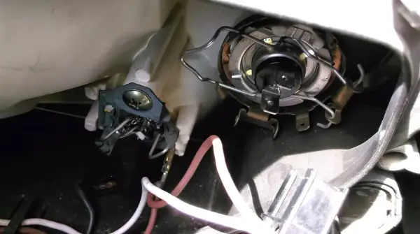 Wymiana żarówki przód Mitsubishi Colt. Widoczny mechanizm mocowania żarówki i przewody.