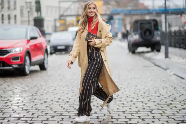 Frau in Beige-Trenchcoat, rotem Rollkragenpullover und gestreiften Hosen, die zeigt, wie man einen Trenchcoat kombinieren kann.