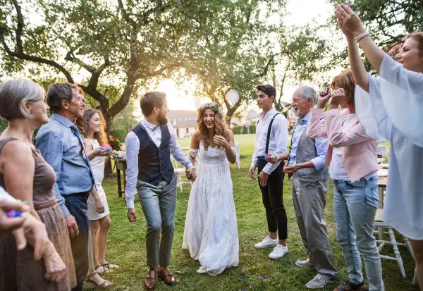 Ein glückliches Brautpaar, schick legere gekleidet, wird von seiner Familie im Garten gefeiert.
