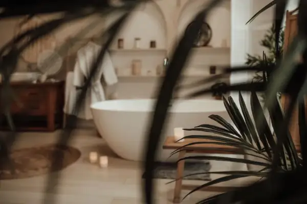 Une baignoire îlot blanche dans une **chaleureux salle de bain zen**. Un peignoir blanc est suspendu, des bougies allumées et des plantes apportent une touche de sérénité.