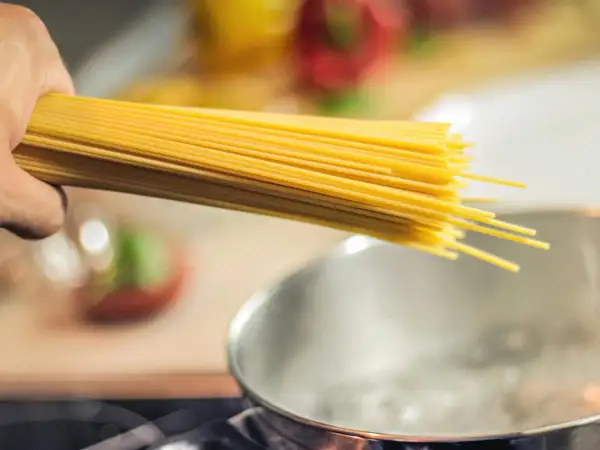 Dłoń trzymająca pęczek spaghetti nad gotującą się wodą. Zastanawiasz się, jaki makaron ma najmniej kalorii?
