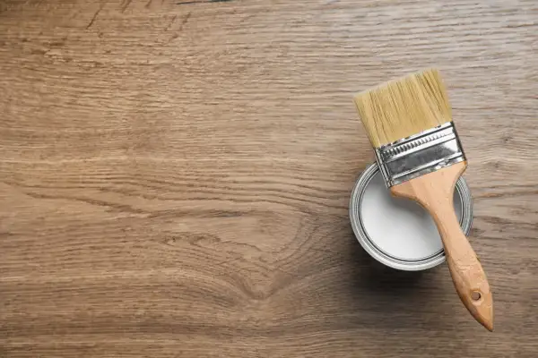 Pennello e barattolo di vernice bianca su fondo in legno, pronti per iniziare a come verniciare un mobile in legno.