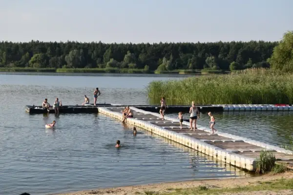 Ludzie odpoczywają i kąpią się na pomoście przy zalewie Murowaniec. W tle las i trzciny.