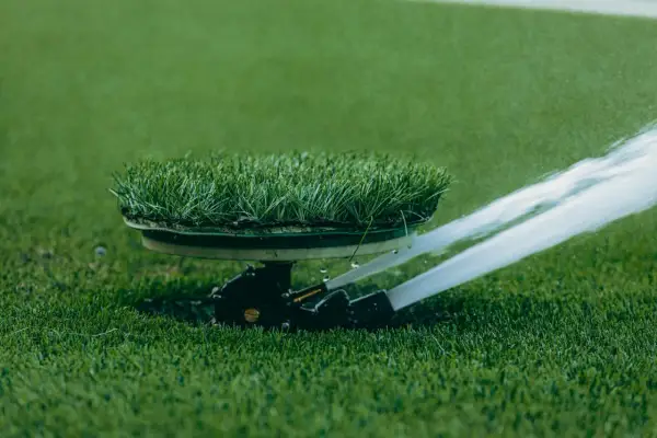 Automatyczne podlewanie trawnika na boisku sportowym. Zraszacze równomiernie rozprowadzają wodę po zielonej murawie.