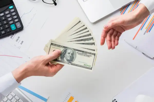 Przekazanie pieniędzy na rachunek bankowy. Dłonie przekazują stos banknotów 100 dolarowych.