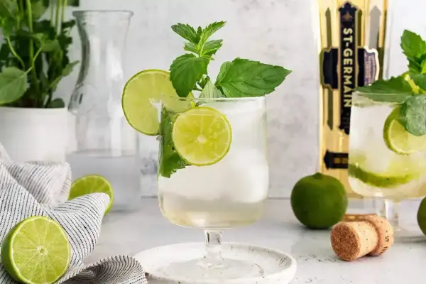 Orzeźwiający Hugo Spritz z limonką i miętą, idealny na letnie popołudnie. Obok butelka St-Germain.
