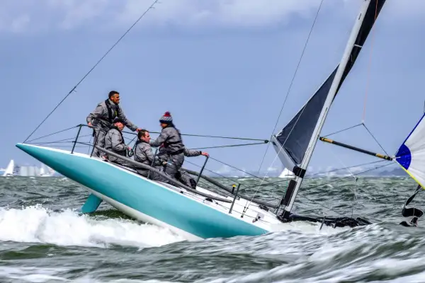Equipaggio su barca a vela con spinnaker in azione, solcando onde agitate.