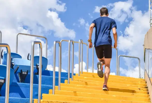 Un homme en tenue de sport monte des escaliers jaunes, un entraînement de renfo course à pied sous un ciel bleu.
