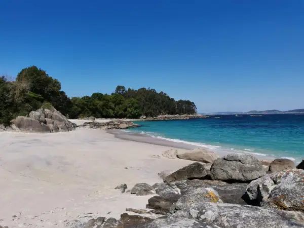 Arena blanca, aguas turquesas y rocas salpican la **playa de Castiñeiras**, un rincón idílico bajo un cielo azul intenso.