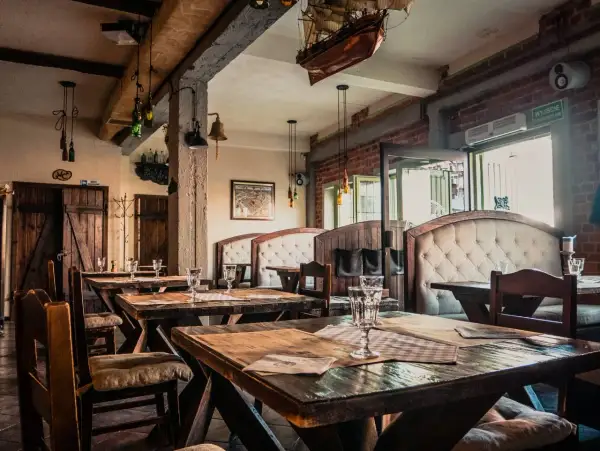 Wnętrze restauracji z drewnianymi stołami i wygodnymi kanapami. Na ścianie wisi model statku, nawiązujący do morskiego klimatu, jak w gdańskim bowke.