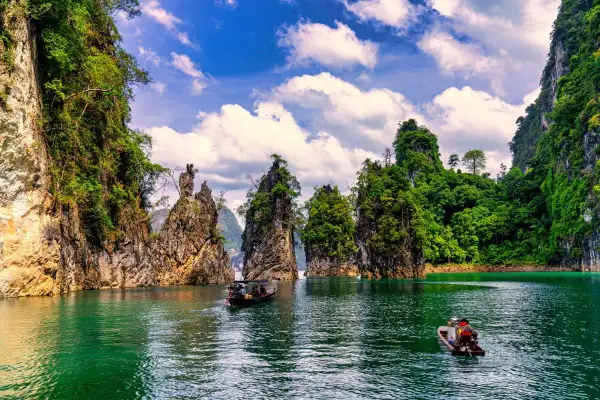 Khao Sok nationalpark med sina dramatiska kalkstensklippor och smaragdgröna vatten. Två små båtar glider fram på sjön.