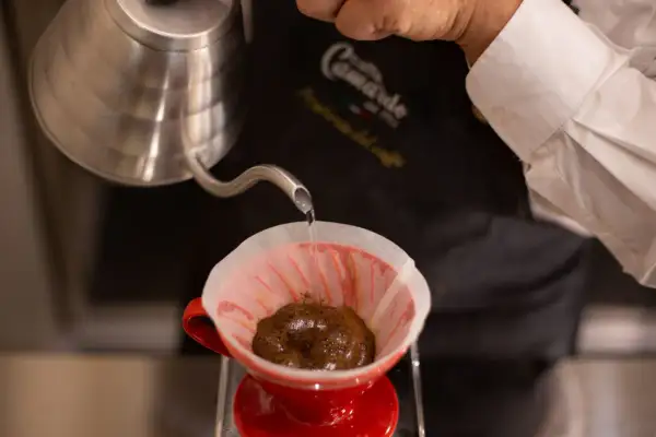 Versando acqua calda su caffè macinato in un filtro di carta rosso, per preparare un caffè filtro. Ecco come funziona la caffettiera americana.