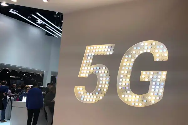 Wielkie, podświetlane litery "5G" na ścianie, symbolizujące przyszłość technologii. W tle widać ludzi i stoiska targowe.
