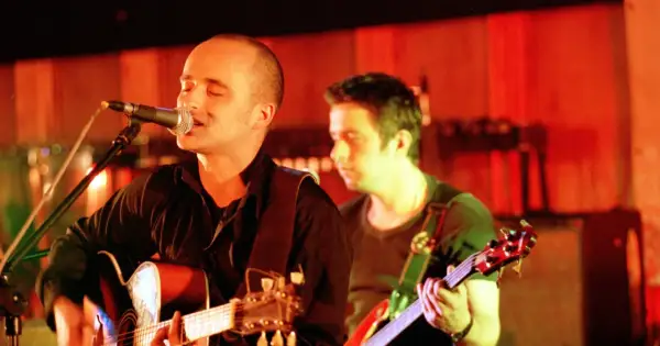 Wokalista z gitarą śpiewa do mikrofonu, i nawet kiedy będę sam, czuje wsparcie kolegi z zespołu.