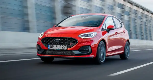Czerwony Ford Fiesta ST pędzi po drodze, błyszcząc w słońcu.
