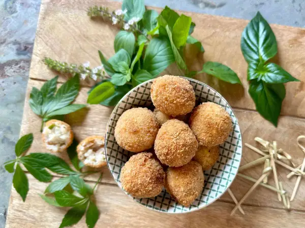 Goldbraune Arancini in einer Schale, umgeben von frischem Basilikum. Was isst man zu Arancini? Oft mit einer leichten Sauce oder einfach so!
