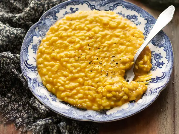 Un cremoso risotto alla zucca, servito su un piatto decorato, con una forchetta che affonda nel piatto.
