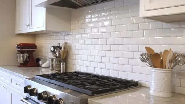 A clean kitchen backsplash installation with white subway tiles, a red stand mixer, and cooking utensils.