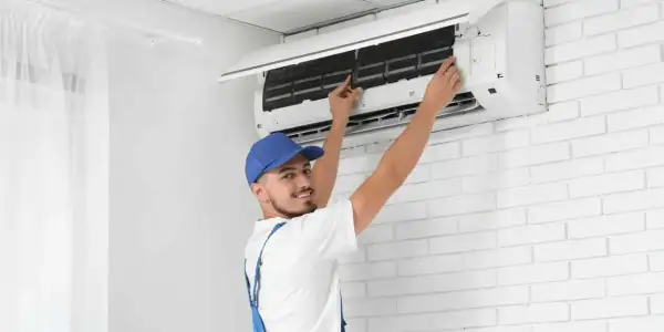 Tecnico con cappellino blu esegue la sanificazione aria condizionata, controllando i filtri per un'aria più pulita.
