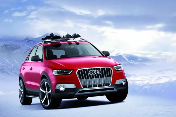 Czerwony Audi Q1 z nartami na dachu gotowy na zimową przygodę w górach.