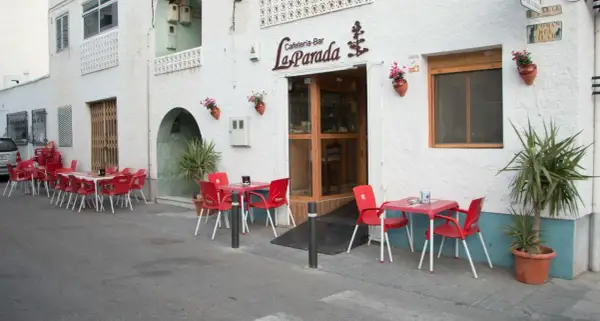Cafetería-Bar "La Parada", un lugar acogedor donde comer en Níjar. Mesas rojas y sillas esperan en la acera.