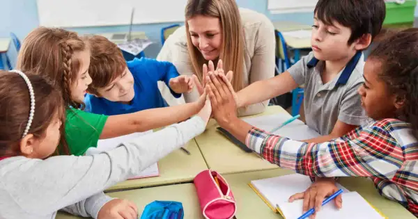 Niños y maestra celebran con un choque de manos, fomentando la motivación en el aula.