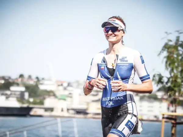 Uśmiechnięta sportsmenka w stroju do triathlonu, biegnie z kubkiem wody. To właśnie triathlon co to za dyscyplina sportu!