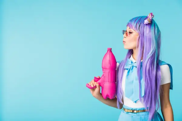 Dziewczyna w peruce w stylu kawaii z fioletowymi i niebieskimi włosami trzyma różowy pistolet na wodę.