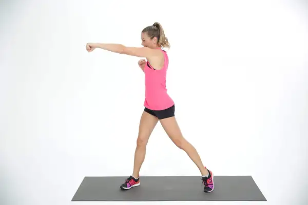 Woman in pink tank top and black shorts performs an undercut punch on a mat.