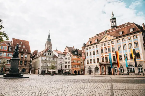 Blick über den Marktplatz der Coburg Altstadt mit historischen Gebäuden, einem Denkmal und Fahnen.