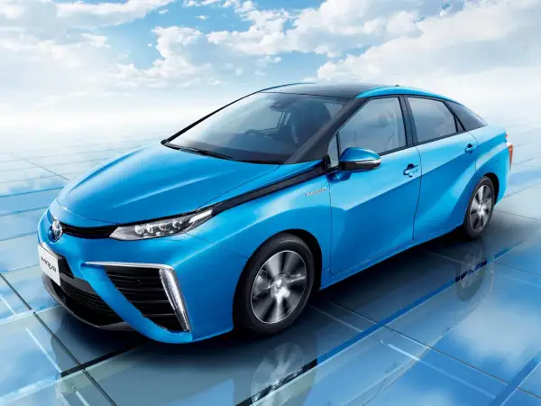 Niebieski samochód Toyota Mirai na tle błękitnego nieba z chmurami.