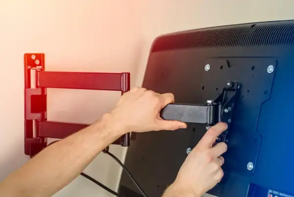 Montaż telewizora na ścianie. Ręce przykręcają uchwyt do ekranu, przygotowując mocowanie telewizora na ścianie.