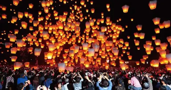 Tysiące lampionów unosi się na nocnym niebie, tworząc magiczny widok podczas święta lampionów. Tłum ludzi obserwuje to widowisko.
