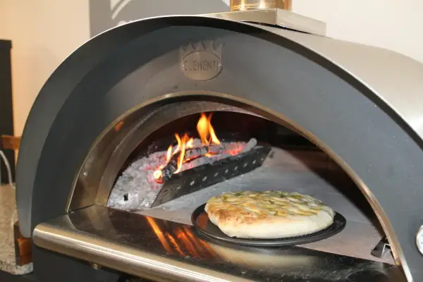 Una crescia dorata pronta per essere infornata in un forno a legna Clementi, con fiamme vive che creano l'atmosfera perfetta per la ricetta.
