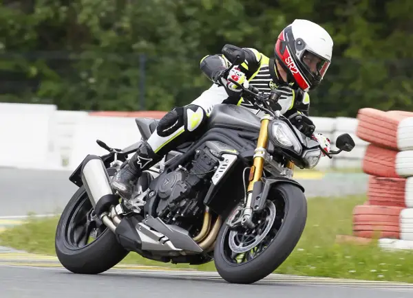 Motocyklista w kasku i kombinezonie pochyla się na torze wyścigowym na motocyklu Triumph Speed Triple.