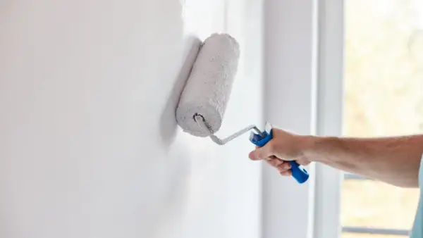 Mano aplica pintura aterciopelada blanca a una pared con un rodillo.