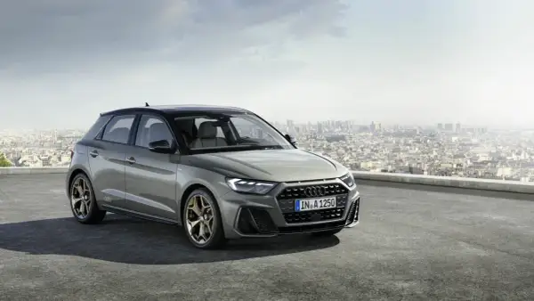 Szary Audi RS1 z brązowymi felgami stoi na dachu z widokiem na miasto.
