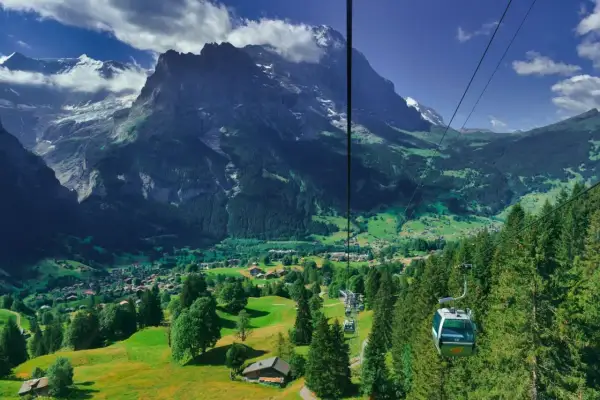 Widok z kolejki linowej na dolinę Grindelwald, z górami w tle i zielonymi łąkami.