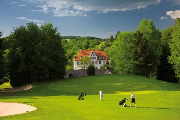 Zwei Golfer auf dem grünen Rasen des Golfclubs Schloss Georghausen, im Hintergrund das malerische Schloss.
