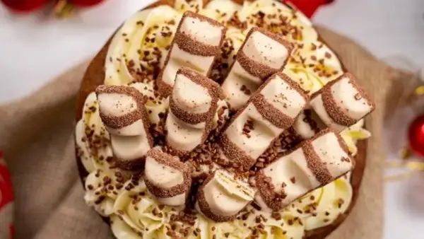 Tarta decorada con crema amarilla y trozos de tarta kinder bueno, espolvoreada con virutas de chocolate.