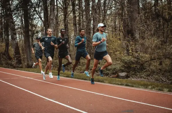 Cinq coureurs s'entraînent sur une piste, leurs foulées rythmées par un entraînement de fractionné course intense.