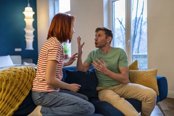 Ein Paar sitzt auf einem Sofa und gestikuliert lebhaft. Sie scheinen sich nach einem Streit wieder zueinander zu finden, die Spannung weicht langsam der Versöhnung.