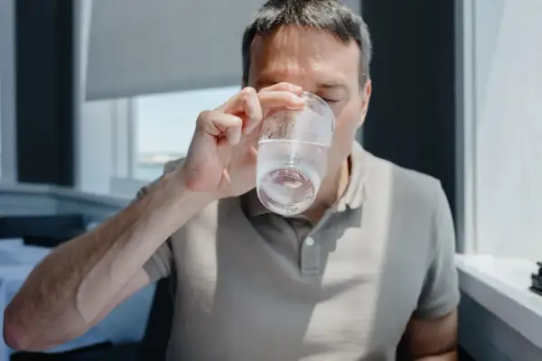 Mężczyzna pije wodę, zastanawiając się, ile pić wody, żeby schudnąć. Woda jest kluczem do zdrowia i metabolizmu.