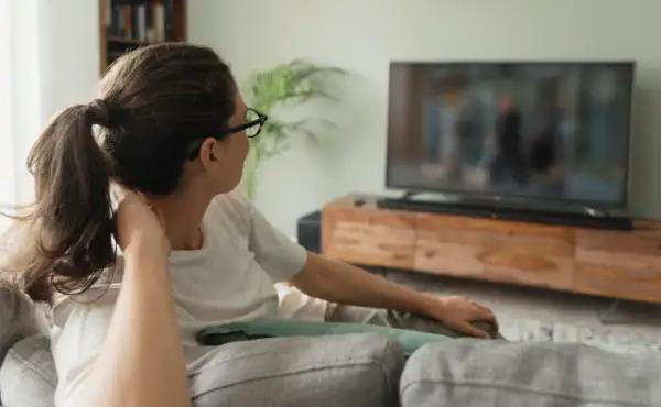 Kobieta w okularach relaksuje się na kanapie, oglądając film na dużym telewizorze 60 cali. Wymiary ekranu idealnie pasują do salonu.