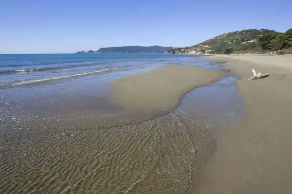 Le **spiagge** dorate dell'**Argentario** incontrano il mare cristallino, con un ruscello che serpeggia sulla **sabbia**.