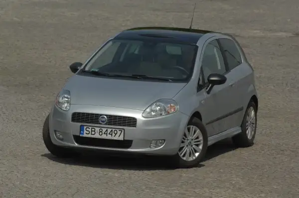 Srebrny Fiat Grande Punto z czarnym dachem i nowymi żarówkami, gotowy do jazdy po brukowanej nawierzchni.