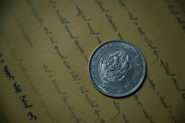 Srebrna moneta bulionowa z wizerunkiem smoka, leżąca na pożółkłym papierze z orientalnym pismem.