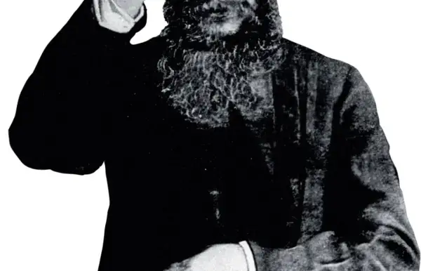 Grigorij Rasputin, z charakterystyczną brodą, wznosi rękę w geście błogosławieństwa lub pozdrowienia.